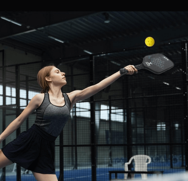 피클볼 라켓을 든 여성이 노란색 피클볼을 치고 있다.